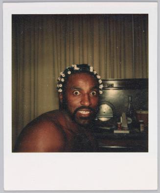 [Man wearing curlers in his hair, eyes wide open and baring his teeth]