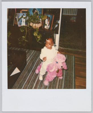 [Toddler sitting on pink sheep toy on carpet]
