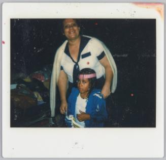 [Woman with cardigan set over her shoulders standing with little girl wearing pink headband]
