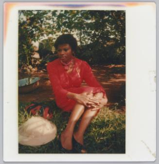 [Woman wearing red dress sitting and holding her knees on grass]
