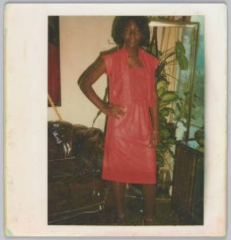 [Woman wearing matching pink outfit standing with hand on hip in front of mirror and plant]
