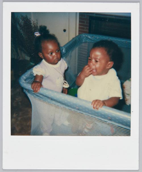 [Two toddlers in playpen, toddler on right is crying with hand over mouth]
