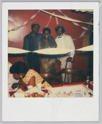 [Two men and a woman standing together and smiling at party, streamers hung on walls]
