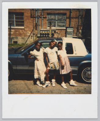 [Three girls posing in floral dresses and skirts standing in front of car]
