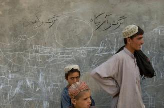 Afghan civilians stand by a wall covered in graffiti depicting machine guns and two anti-coalition slogans in Pashto saying "Death for London" and Death for America" in an area recently pacified and secured by the US Marines from the 24th Marine Expeditionary Unit (MEU) and British Forces in Garmsir District, Helmand Province, Afghanistan. Garmsir has been a haven for insurgents for the last several years. Earlier this year the Marines cleared the area after a period of heavy fighting and recently handed over control to British Forces