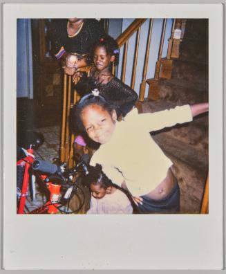 [Girl in white shirt hanging off staircase railing, two more girls on staircase, red bike to the left]