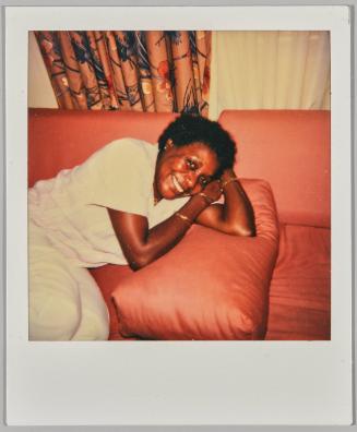 [Woman in white outfit leaning on couch, curtained window behind]