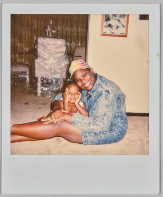 [Woman in tie dye baseball cap holding a child and sitting on the floor]