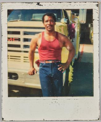 [Man in red tank top and brown leather belt standing in front of GMC truck]