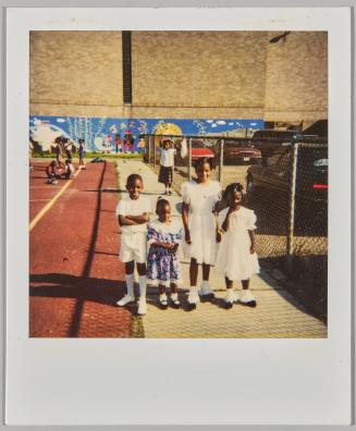 [Three children dressed in white and girl in floral dress standing outside, wall mural in background]