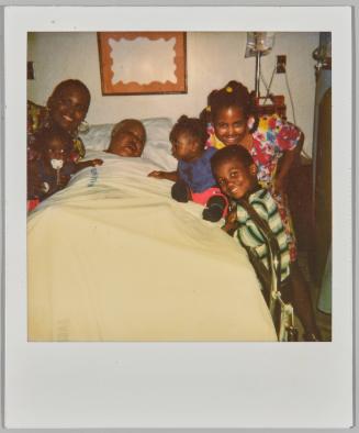 [Adult asleep in hospital bed, woman and baby on left and three children on the right]