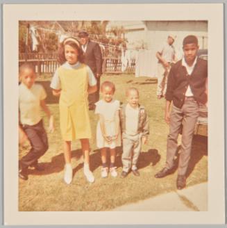 [Group of children standing on lawn, older girl on left in yellow jumper and yellow hairband]