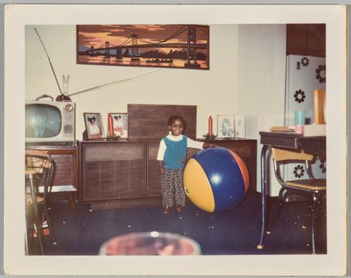 [Young girl smiling and standing next to large exercise ball in living room]