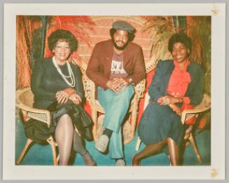 [A man and two women each sitting on a wicker chair]