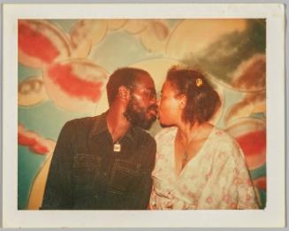 [Man and woman going in for a kiss, standing in front of painted mural on wall]
