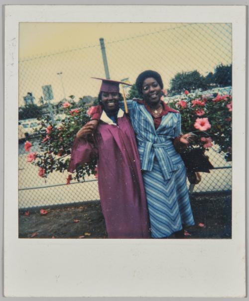 [Woman in blue striped outfit with arm around young woman in maroon graduation cap and gown]

