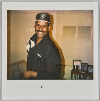 [Man smiling wearing black Adidas jacket and baseball cap]
