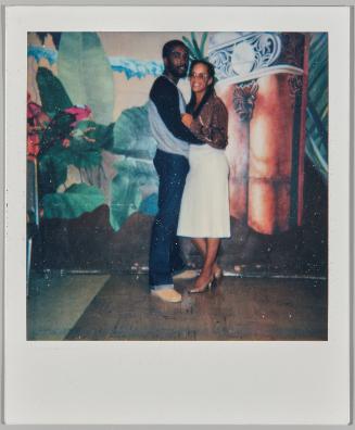 [Man and woman holding each other and standing in front of painted mural on back wall]
