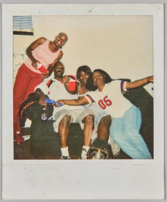 [Three women and a man sitting on couch with red plastic cups and alcoholic beverages, woman on right has arms outstretched]

