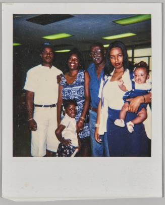 [Family posing, woman on right holding baby on one arm]
