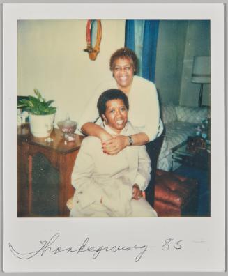 Thanksgiving '85 [Woman sitting on chair and smiling while other woman hugs her around the shoulders from behind]
