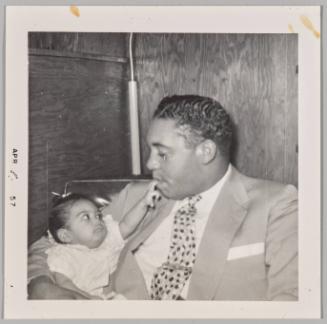 [Man holding baby in arms, baby placing two fingers on his lips]
