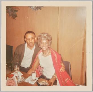 [Woman in red sequinned cardigan smiling with man at table]

