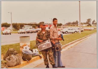 [Two men posing and holding boomboxes]

