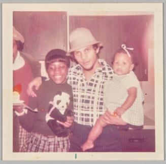 [Man in beige hat with arm around woman and holding baby girl]
