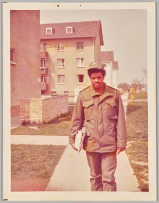 [Man in green uniform holding binders at his side walking down sidewalk]
