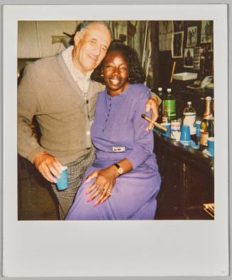 [Man holding a cigar with arm around woman wearing purple]
