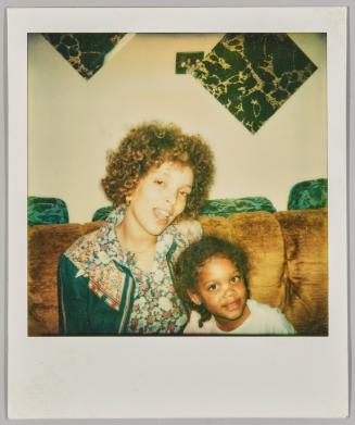 [Woman and little girl sitting on brown velvet couch]
