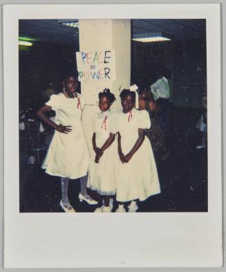 [Three girls in white dresses standing in front of "Peace is Power" sign]

