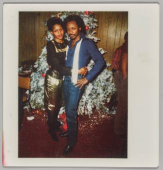 [Man and woman dressed formally embracing in front of Christmas tree]
