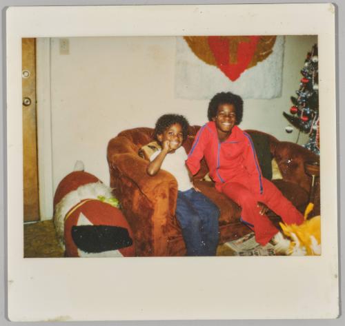 [Two boys smiling on couch with Christmas tree to right]
