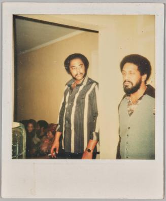 [Two men in home, man on left smoking cigartte, man on right blinking]
