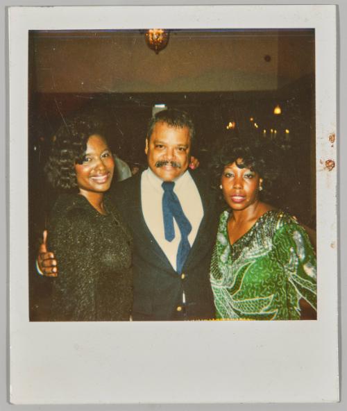 [Man and two women smiling and dressed formally under low lighting]
