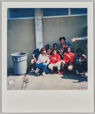 [Seven adolescents crouching on concrete beside garbage can]
