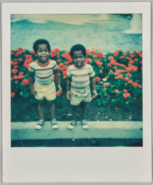 [Two little boys standing in front of garden of red roses]
