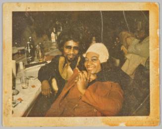 [Man in gold detailed dress shirt holding hands with woman with blue eyeshadow]
