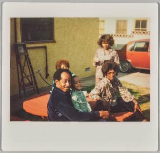 [Three women, a man, and girl seated at red picnic table]
