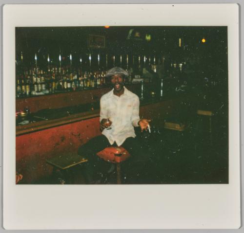 [Young man on seated at bar holding cigarette and glass with mouth open]
