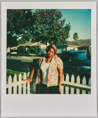 [Woman in floral top leaning on white pickett fence]
