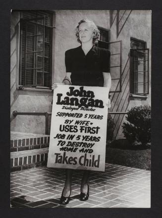Woman holding up a sign - "John Langan, dialogue director, supported 5 years by wife…"