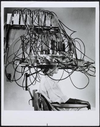 A patient sits underneath a complicated contrivance with dangling wires called a multidetector which can pinpoint a brain tumor.