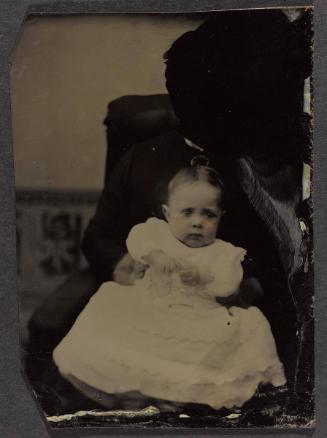 Portrait of young child (seated on lap supported by defaced figure)