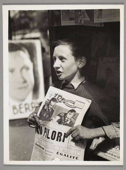 Life goes on in Paris with some changes. A Paris newspaper boy sells French newspapers as well as German magazines.