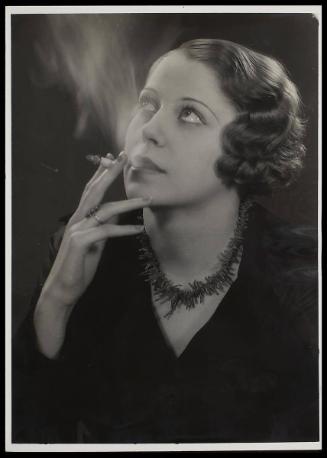 Woman smoking, looking up, wearing a black top and necklace.