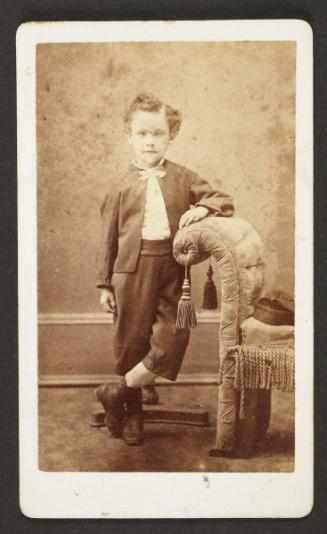 Unknown sitter [portrait of a boy standing next to upholstered bench]