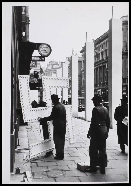 A man manoeuvring a large Swastika sign, in the street.
